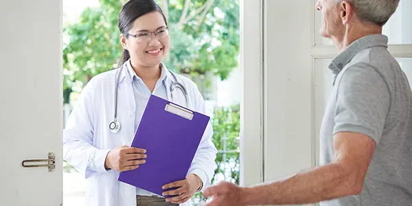 Profissional de saúde entrando em casa de paciente para realizar o atendimento médico domiciliar