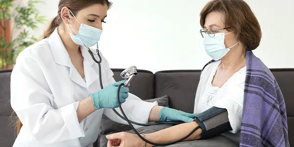 Médica em atendimento domiciliar aferindo pressão de paciente.