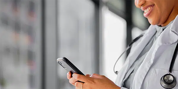 Médica sorridente com estetoscópio no pescoço digita no celular
