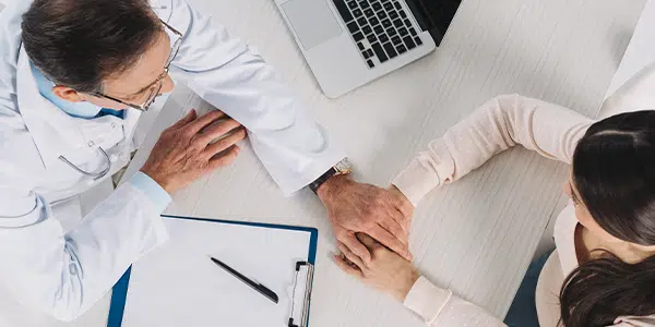 Médico colocando sua mão em cima da mão de uma paciente, em sinal de apoio e força.