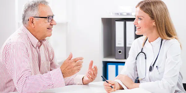 Médica conversando com paciente homem, seguindo as normas de metas internacionais de segurança do paciente.