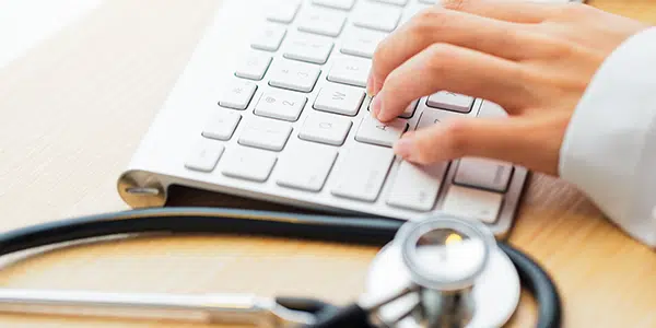 médico digita no teclado com estetoscópio ao lado