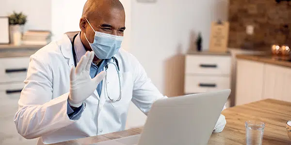 Médico de máscara e luva atende por telemedicina