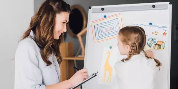 Psicóloga fazendo anotações enquanto menina desenha numa anamnese psicológica infantil