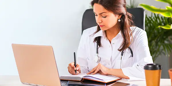 Médica em mesa com café e notebook