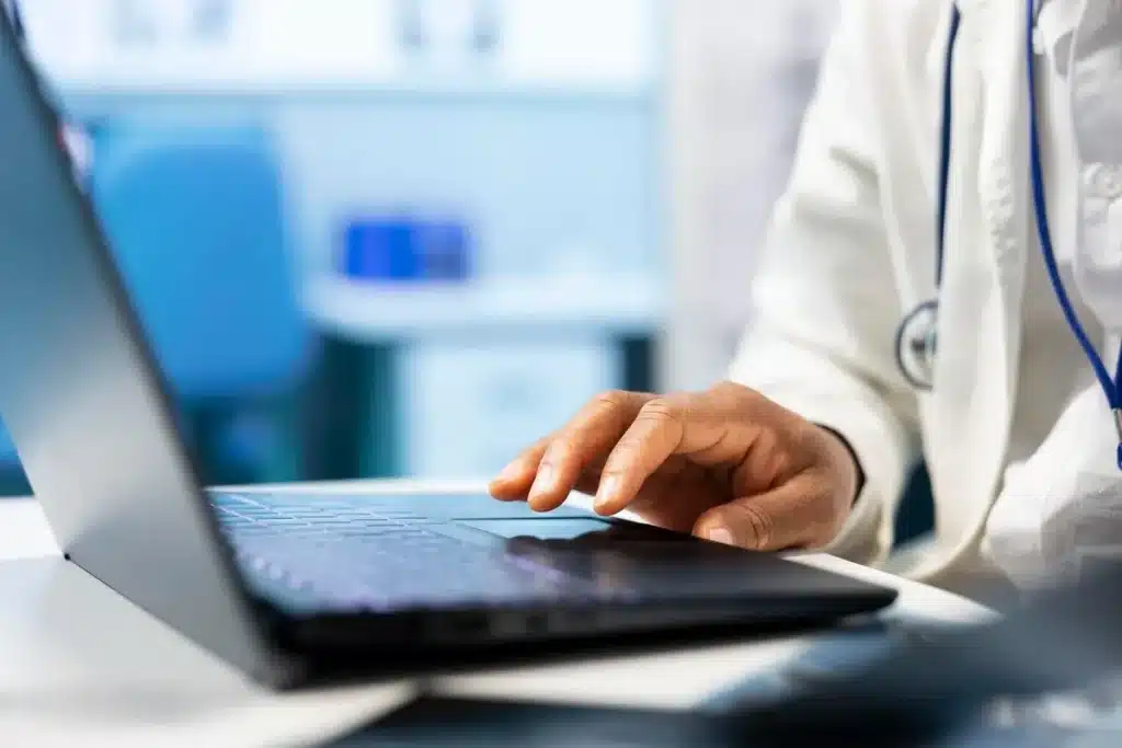 Mãos de médico em notebook ilustram softwares médicos